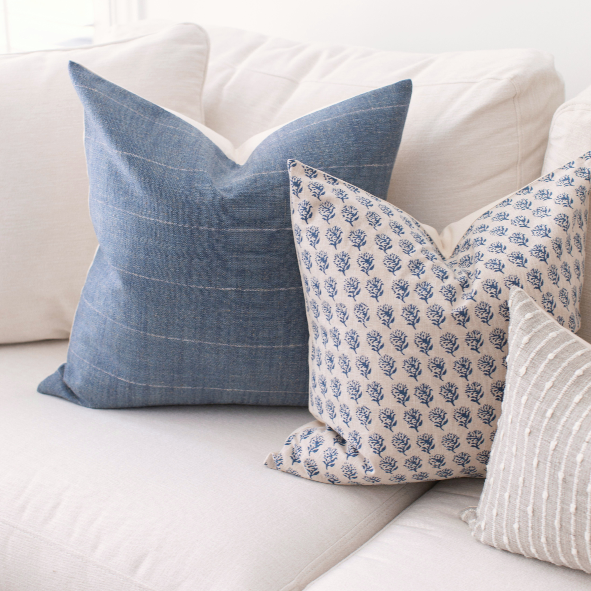 Three decorative pillows on a white couch with blue and white patterns.