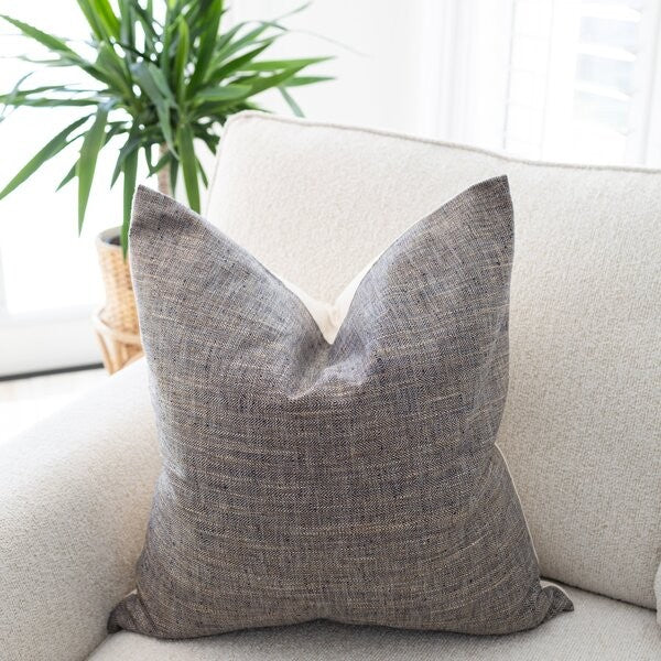 Gray textured pillow on a beige sofa with a plant in the background