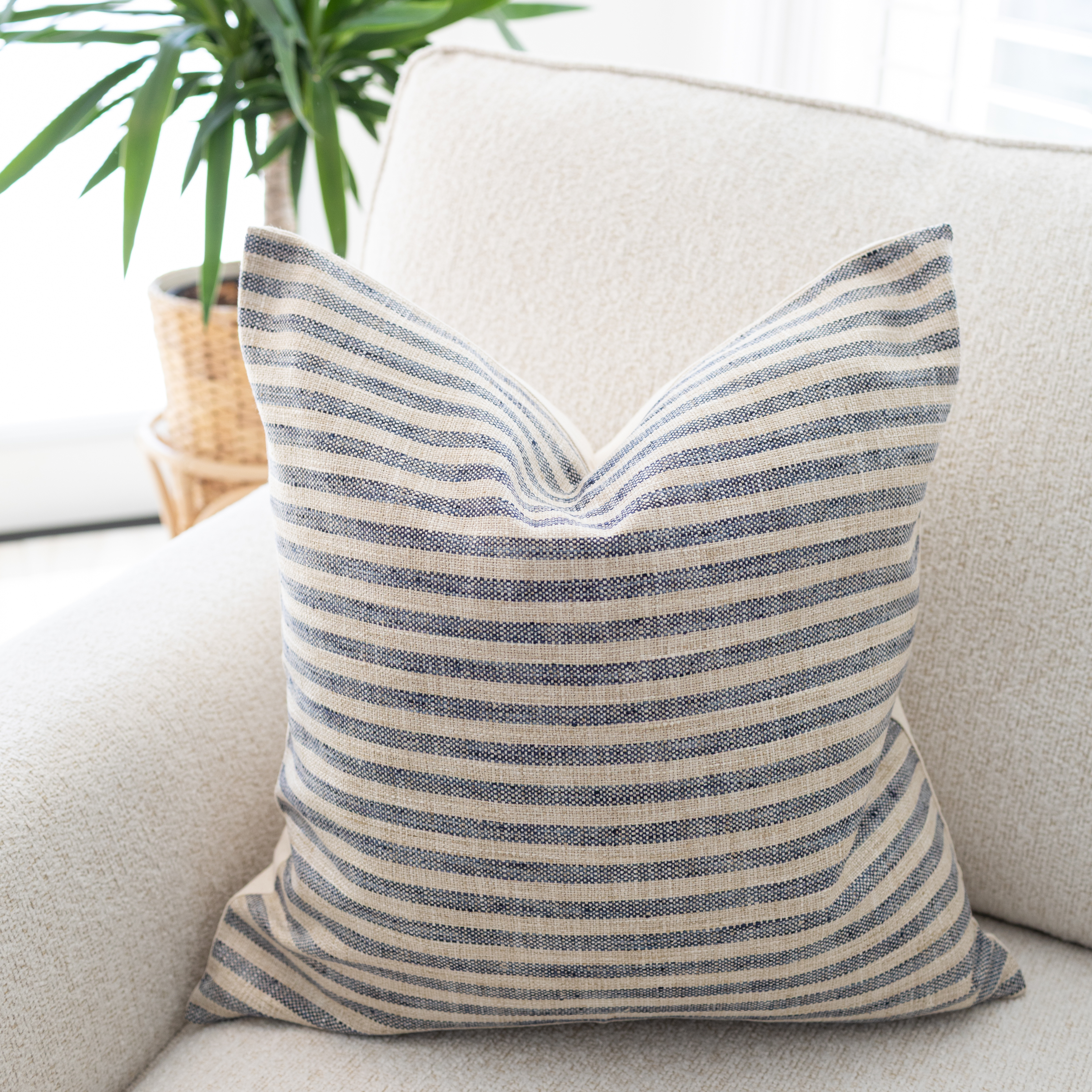 Striped pillow on a beige sofa with a plant in the background