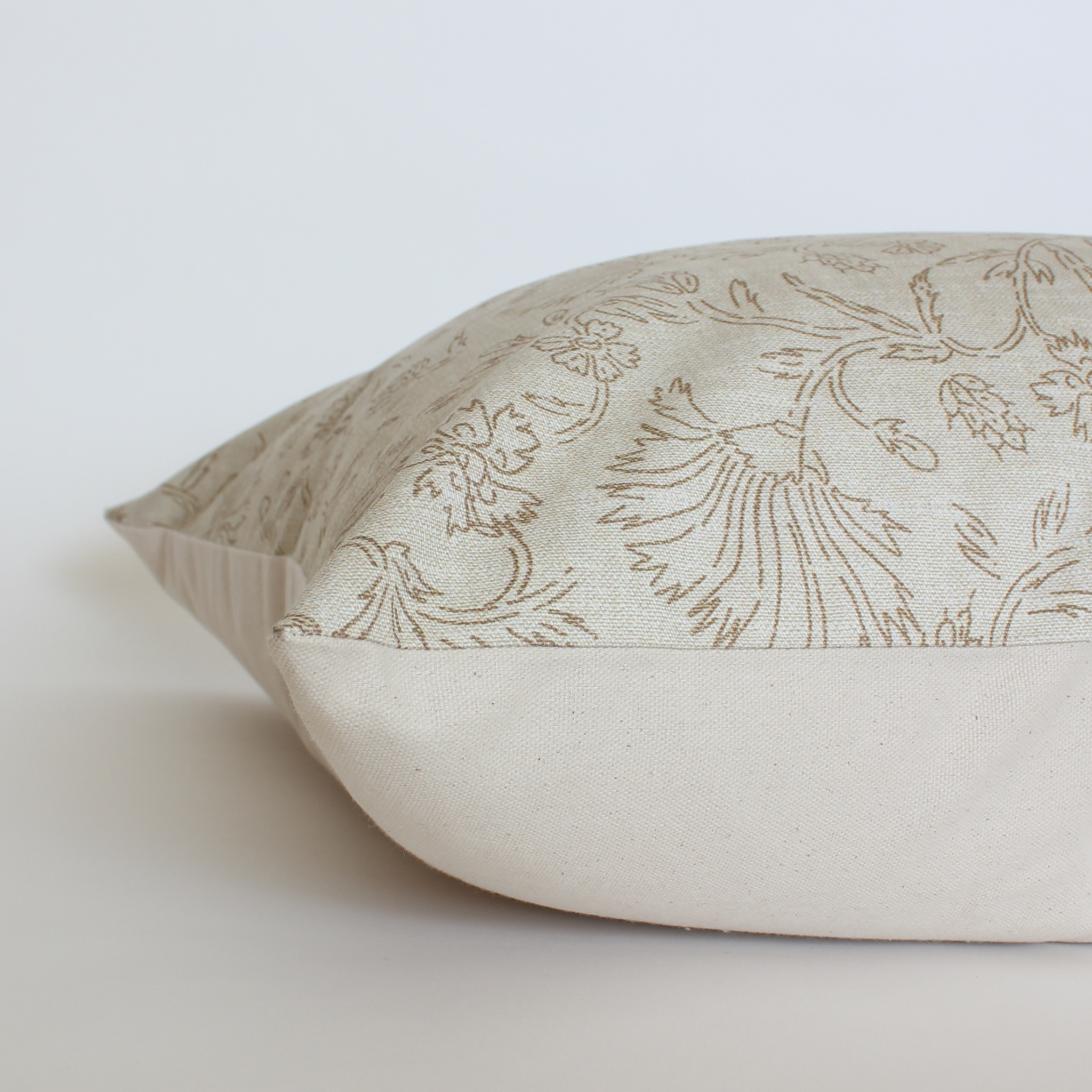 Angled view of cream botanical throw pillow cover with taupe floral vine detail, neutral home decor