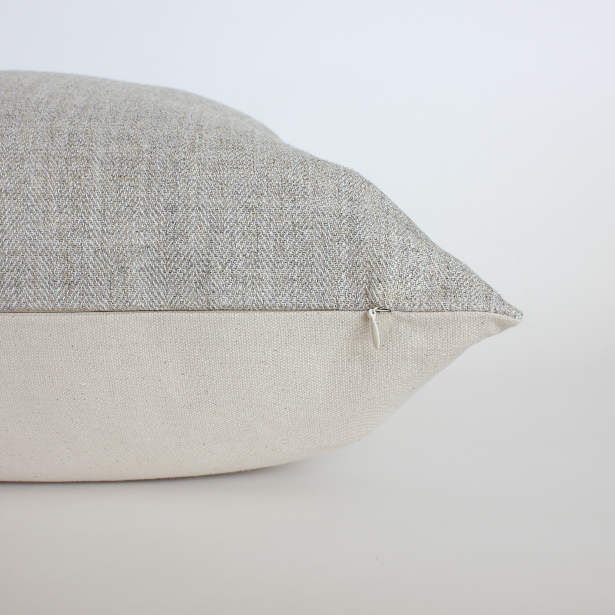 Close up of gray herringbone pillow cover showing cream canvas back and zipper closure detail