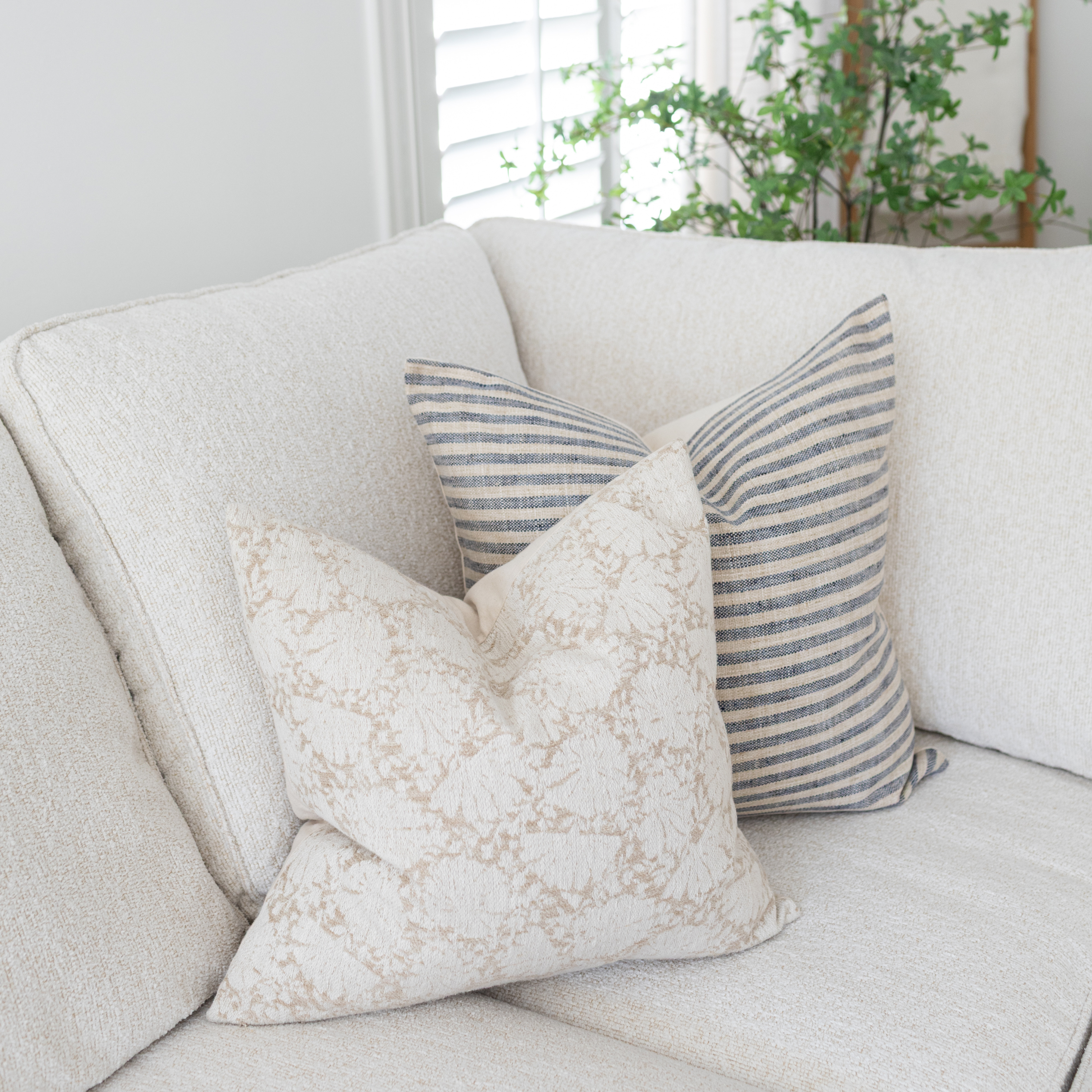 Decorative pillows on a light-colored sofa with a plant in the background