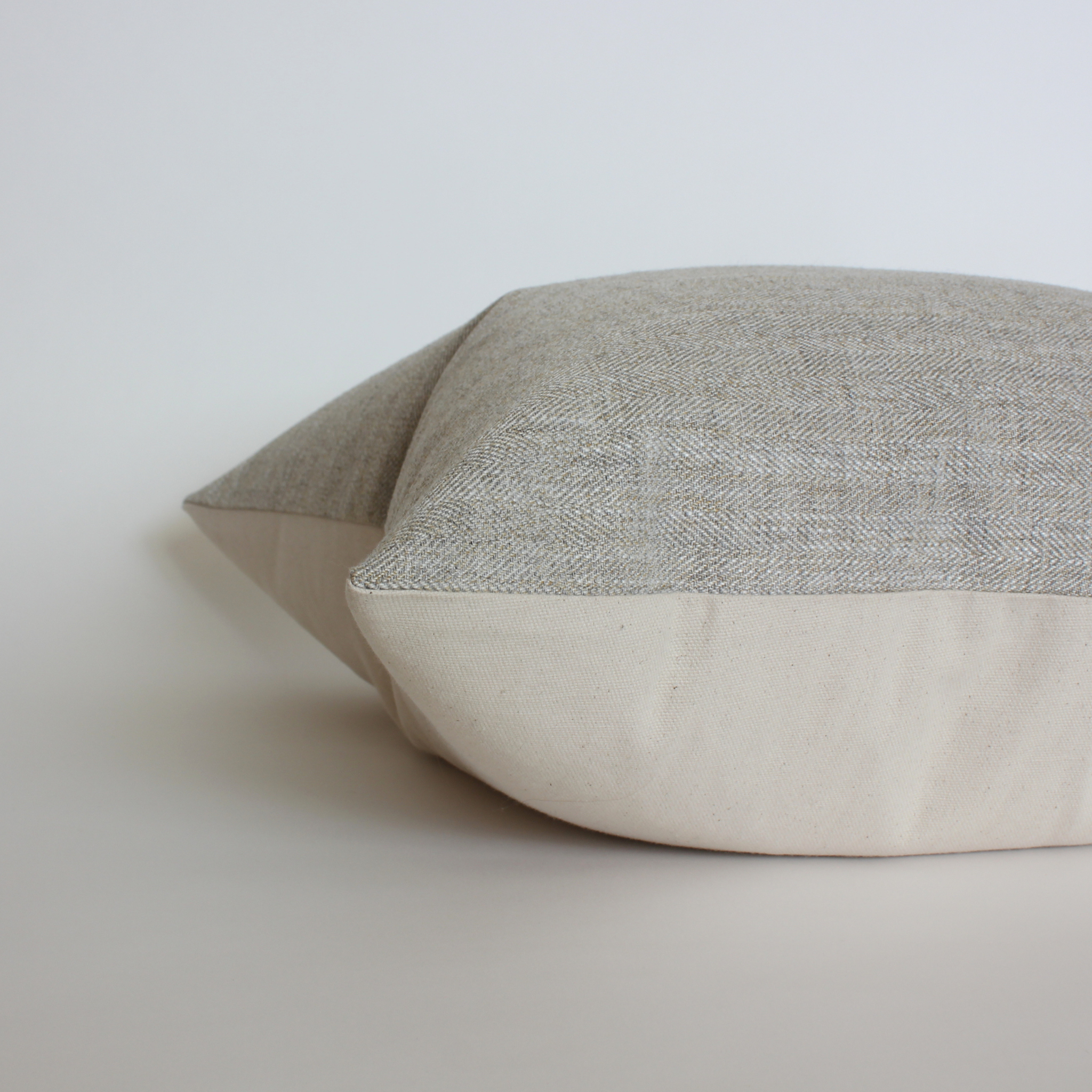 Side view of gray textured throw pillow cover showing cream canvas back and hidden zipper closure