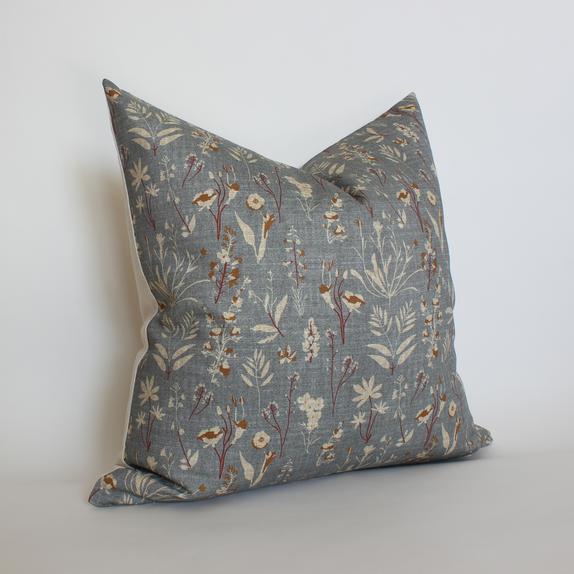 Angled view of blue gray botanical throw pillow with rust and cream floral print, neutral home decor